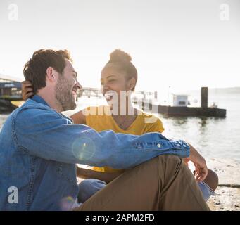 Felice coppia giovane seduto sul molo del lungomare, Lisbona, Portogallo Foto Stock