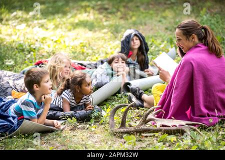 Insegnante di lettura storia per i bambini a scuola, campeggio nella foresta Foto Stock