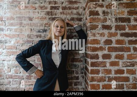 Ritratto di una giovane donna d'affari sicura ad un muro di mattoni Foto Stock