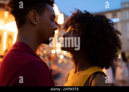 Affettuosa giovane coppia turistica in una giostra illuminata in città al crepuscolo, Firenze, Italia Foto Stock