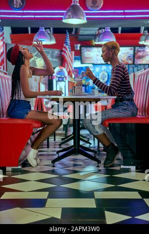 Due donne che condividono un milkshake sul tavolo di un ristorante americano Foto Stock