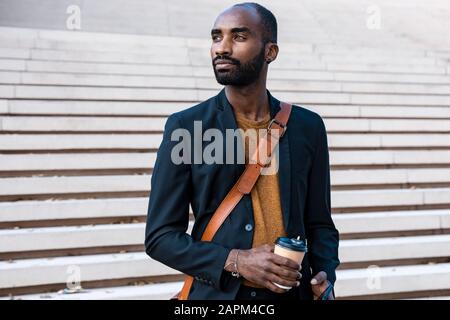 Ritratto di giovane uomo d'affari con bearded con smartphone e caffè per andare a guardare la distanza Foto Stock