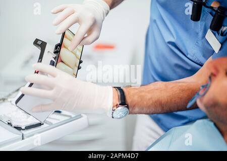 Primo piano del dentista che mostra la foto delle protesi al paziente Foto Stock