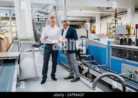Due uomini d'affari che discutono di carta in una fabbrica Foto Stock