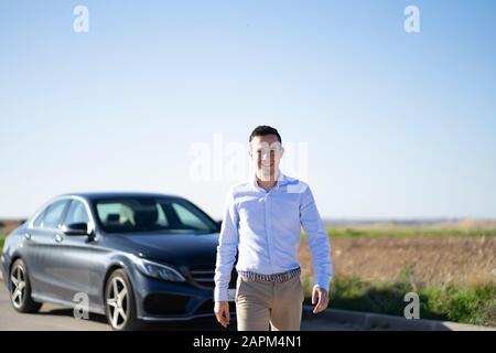 Ritratto di giovane uomo d'affari sorridente con auto su strada di campagna Foto Stock