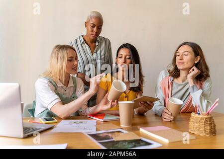 Donne d'affari che hanno una riunione in ufficio che lavora su tazze riutilizzabili Foto Stock