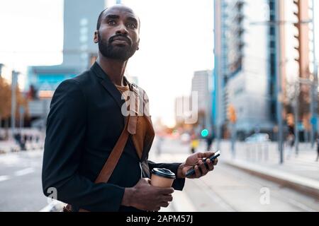 Ritratto di giovane uomo d'affari con caffè da andare e smartphone guardando a distanza Foto Stock