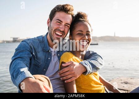 Ritratto di felice giovane coppia seduto sul lungomare, Lisbona, Portogallo Foto Stock