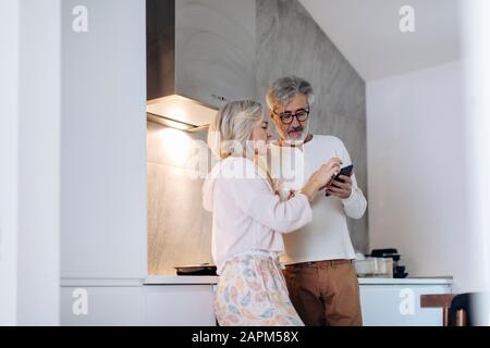 Coppia matura utilizzando cellulare in cucina a casa Foto Stock