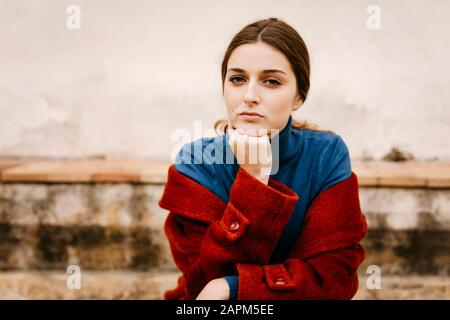 Primo piano ritratto di donna con turtleneck blu pullover e cappotto rosso, mano sul mento Foto Stock