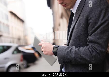 Vista del raccolto di un giovane uomo d'affari con un tablet digitale che guarda lo smartwatch Foto Stock