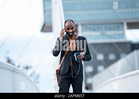 Sorridente giovane uomo d'affari che usa smartphone e cuffie all'aperto Foto Stock
