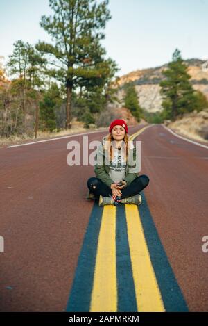 Ragazza seduto sulla strada nel Zion National Park nello Utah sudoccidentale vicino alla città di Springdale Foto Stock