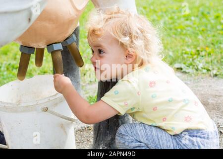 Carina ragazza bionda ad apprendere come il latte di una mucca sul simulatore di mungitura. Foto Stock