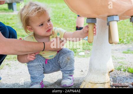 Carina ragazza bionda ad apprendere come il latte di una mucca sul simulatore di mungitura. Foto Stock