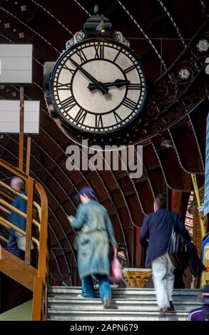 Passeggeri che scalano i gradini per il ponte pedonale alla stazione ferroviaria di York con grande orologio della stazione e struttura sul tetto sopra. Foto Stock