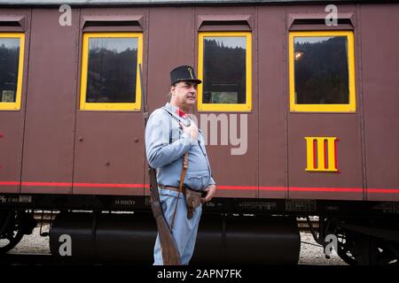 Most na Soči, Slovenia, 4 novembre 2017: Attore che gioca un soldato austro-ungarico che accompagna l'arciduca austriaca Franz Ferdinand si trova di fronte a un'auto da passero di un treno museale di cento anni che corre sulla linea ferroviaria di Bohinj (Transalpina). La linea fu costruita tra il 1900 e il 1906 come il più breve collegamento tra l'Impero Austro-Ungarico e il Mare Adriatico di Trieste (Italia). Fu inaugurato nel 1906 dall'arciduca Francesco Ferdinando che viaggiò anche su questa linea. La rievocazione dell'evento è ora parte di un tour in treno. Foto Stock