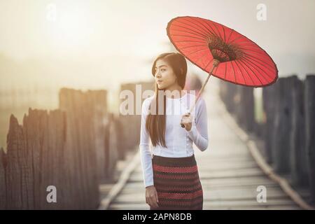 Donne birmane in abito tradizionale birmano con ombrello rosso su U bein ponte Mandalay, Myanmar. Foto Stock