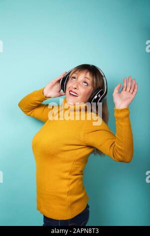 Donna simpatica con cuffie che ascoltano musica e ballano su sfondo blu. Immagine isolata. Foto Stock