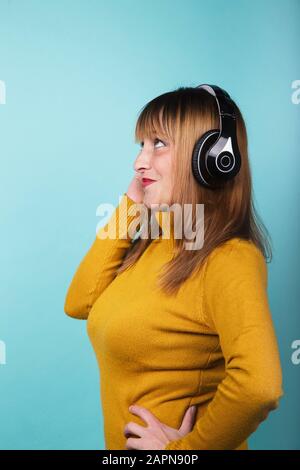 Donna in giallo pullover sorridente con cuffie ascoltare musica sorridente su sfondo blu. Immagine isolata. Foto Stock