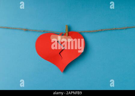 Rottura del cuore di carta appeso alla corda. Cuore rosso rotto appeso sulla corda su sfondo blu. San Valentino Foto Stock