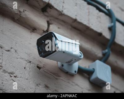 Telecamera CCTV per esterni montata sulla parete di una vecchia casa in mattoni. Nuova telecamera con pellicole protettive sull'obiettivo. Video sorveglianza su una strada della città. Foto Stock