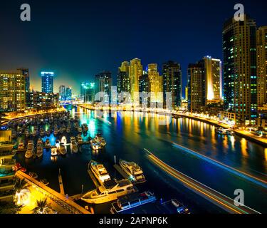 Scena notturna dello skyline della città e delle barche ormeggiate al porto di Dubai Foto Stock