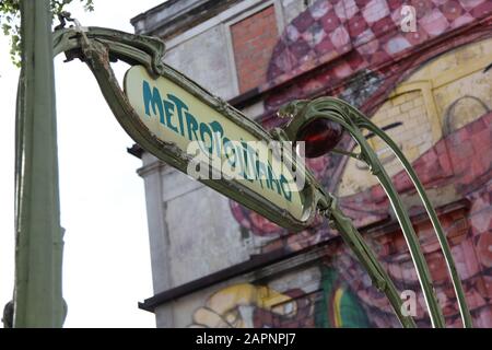 Segnaletica tradizionale per l'ingresso alla metropolitana (metropolitano) con Street art sul lato dell'edificio sullo sfondo di Lisbona, Portogallo Foto Stock