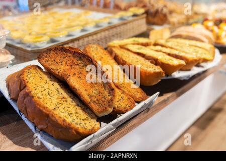 delizioso pane all'aglio appena sfornato con erbe aromatiche, affettato, sul bancone della finestra di un negozio di prodotti da forno, foto da vicino. Foto Stock