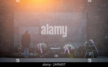 24 gennaio 2020, Polonia, Oswiecim: Al mattino presto, un uomo depone fiori sul muro nero nel cortile tra I Blocchi 10 e 11 dell'ex campo di concentramento di Auschwitz I. Le riprese si sono svolte presso la parete Nera fino al dicembre 1943. 27.01.2020 ricorre il 75th anniversario della liberazione del campo di concentramento da parte dell'Armata Rossa. Dal 1940 al 1945, la SS gestiva il complesso con numerosi campi satellite come campi di concentramento e di sterminio. Il numero di coloro che sono stati uccisi ammonta a 1,1 - 1,5 milioni, la maggior parte dei quali ebrei. Auschwitz è il simbolo dell'omicidio di massa industriale e del Th Foto Stock