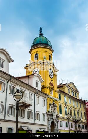 Torre dell'orologio della città barocca dipinta in giallo in una giornata di sole. Colorati vecchi edifici con file di finestre nel centro di Rijeka, Croazia Foto Stock