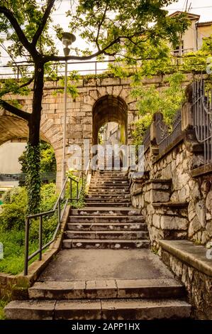 Parte inferiore di Petra Stube, o scala Petar Kruzic, o scala Trsat a Rijeka, Croazia con arco e ponte ferroviario. I gradini in pietra conducono tra i muri Foto Stock