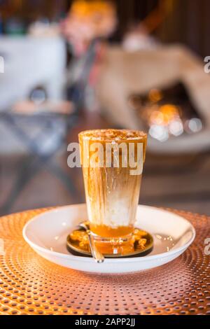 Caffè ghiacciato con latte in bicchieri alti sul tavolo con sciroppo al caramello. Foto Stock