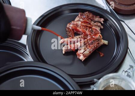 Bistecca alla griglia si trova su un piatto nero rotondo. Bistecca alla griglia si trova su un piatto nero rotondo. I pezzi di bistecca sono innaffati con salsa. Foto Stock