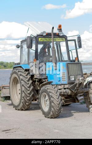 Trattore leggero bielorusso con ugello, benna e martello pneumatico, per la riparazione e la modernizzazione della strada asfaltata. Russia. Foto Stock