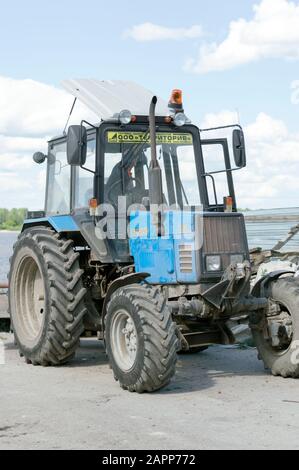 Trattore leggero bielorusso con ugello, benna e martello pneumatico, per la riparazione e la modernizzazione della strada asfaltata. Russia. Foto Stock