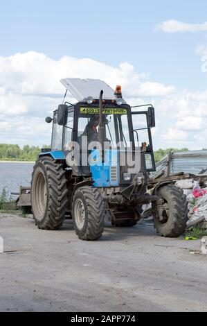 Trattore leggero bielorusso con ugello, benna e martello pneumatico, per la riparazione e la modernizzazione della strada asfaltata. Russia. Foto Stock