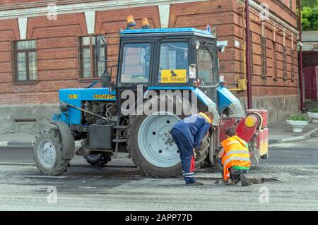 Trattore leggero bielorusso con ugello, benna e martello pneumatico, per la riparazione e la modernizzazione della strada asfaltata. Russia. Foto Stock