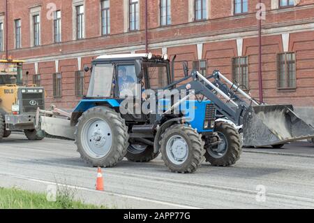 Trattore leggero bielorusso con ugello, benna e martello pneumatico, per la riparazione e la modernizzazione della strada asfaltata. Russia. Foto Stock