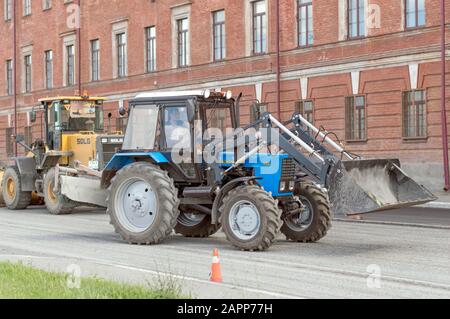 Trattore leggero bielorusso con ugello, benna e martello pneumatico, per la riparazione e la modernizzazione della strada asfaltata. Russia. Foto Stock