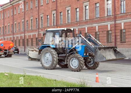 Trattore leggero bielorusso con ugello, benna e martello pneumatico, per la riparazione e la modernizzazione della strada asfaltata. Russia. Foto Stock