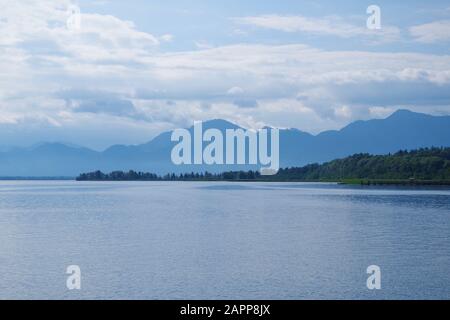 Una vista sulle acque calme del lago Chiemsee (Baviera, Germania). In lontananza, ci sono montagne e isole boscose. Il cielo è molto blu. Foto Stock