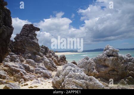 Grande - eroso dall'acqua - rocce su una spiaggia di una piccola isola nell'arcipelago delle Filippine. Paesaggio incantevole con cielo leggermente nuvoloso. Foto Stock