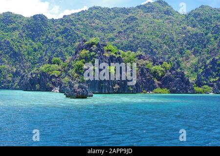 Una grande isola rocciosa nell'arcipelago delle Filippine. L'acqua dell'oceano è calma e leggermente increspata. Il cielo è chiaro e blu. Foto Stock