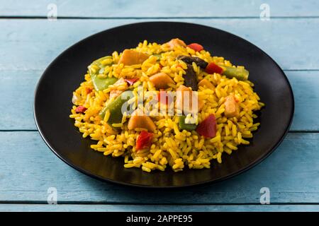 Riso fritto con pollo e verdure in piatto nero su tavola di legno blu Foto Stock