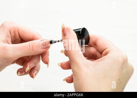 Mani femminili che fanno manicure, smalto per unghie in oro glitter colore su uno sfondo bianco. Concetto di salone di cura della pelle e del chiodo Foto Stock