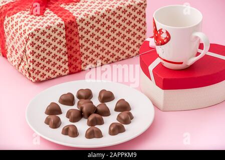 Cioccolato Cuori biscotti in un piatto bianco con scatole regalo e una tazza di caffè per San Valentino su uno sfondo rosa pastello Foto Stock