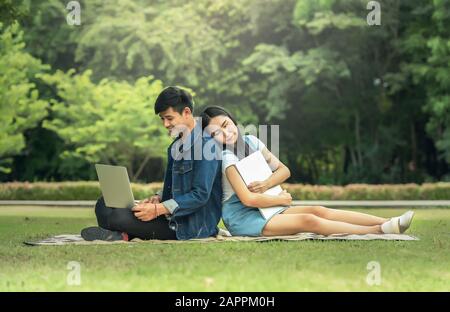 Ritratto di un felice giovane studente seduto sul parco e utilizzando computer portatile all'aperto Foto Stock