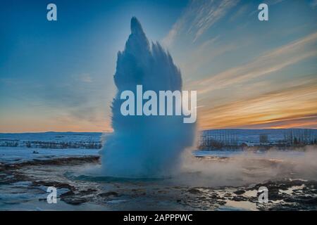 Strokkur Geysir erutta all'alba contro il cielo colorato a Geysir, Haukardalur Valley, Islanda, il freddo giorno invernale in gennaio - effetto hdr Foto Stock