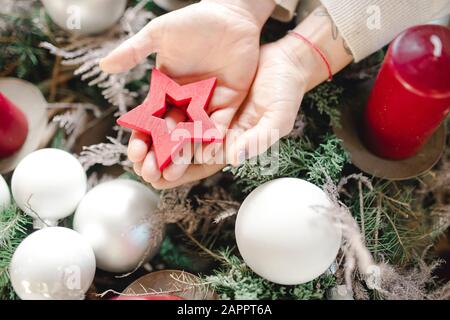 Mano che tiene stella rossa di legno, baubles, candela rossa Foto Stock